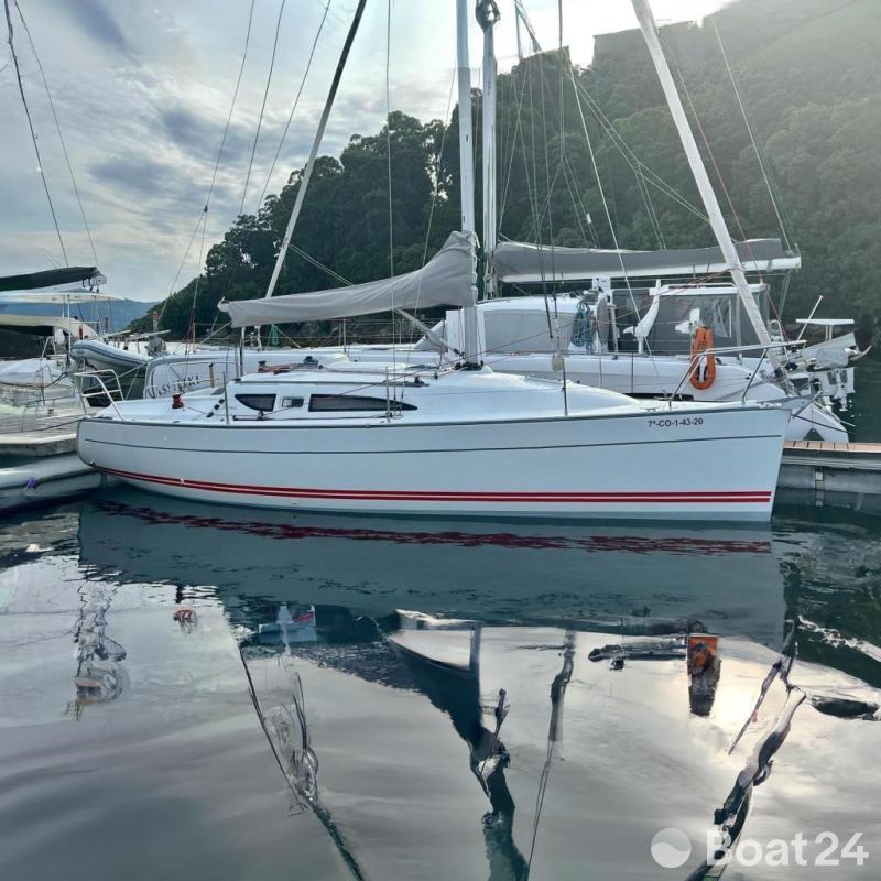 2002 Jeanneau Sun Fast 32i sailboat docked at marina with lush green backdrop.