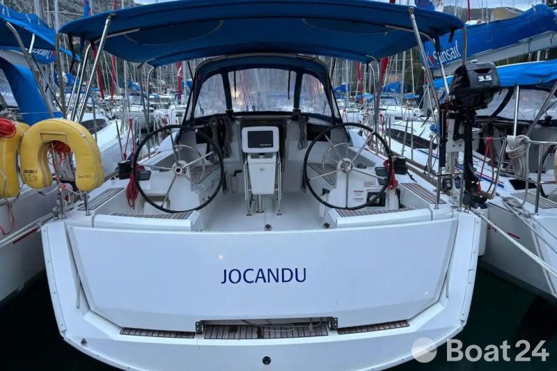 2018 Jeanneau Sun Odyssey 389 sailboat docked, featuring dual steering wheels and blue canopy.