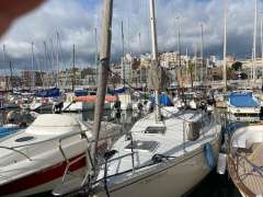 Sailboats docked in a marina, featuring a 1988 Feeling 286 model under cloudy skies.