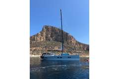 2018 Hanse 588 yacht sailing near rocky cliff under clear blue sky.