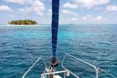Bow of 2013 Beneteau Oceanis 41 sailboat approaching tropical island in clear blue waters.