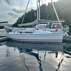 2002 Jeanneau Sun Fast 32i sailboat docked at marina with lush green backdrop.