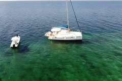 Aerial view of 2008 Leopard 38 catamaran and small boat on clear, green ocean water.
