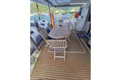 Luxurious Leopard 58 yacht deck with wooden dining table, chairs, and scenic waterfront view.