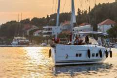 2017 Hanse 588 yacht sailing at sunset near coastal village.