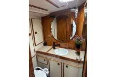 Bathroom interior of 1983 Jeanneau Espace 1000 yacht with wooden accents and round mirror.