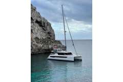 Sailing catamaran Leopard 42, 2021 model, anchored near rocky coastline under cloudy sky.